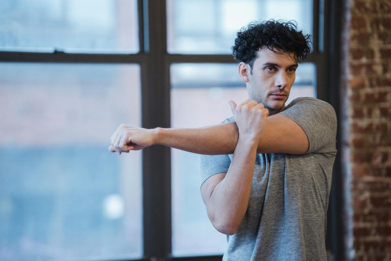 Concentrated male stretching hands while warming up before workout for strengthening body and muscles and looking away